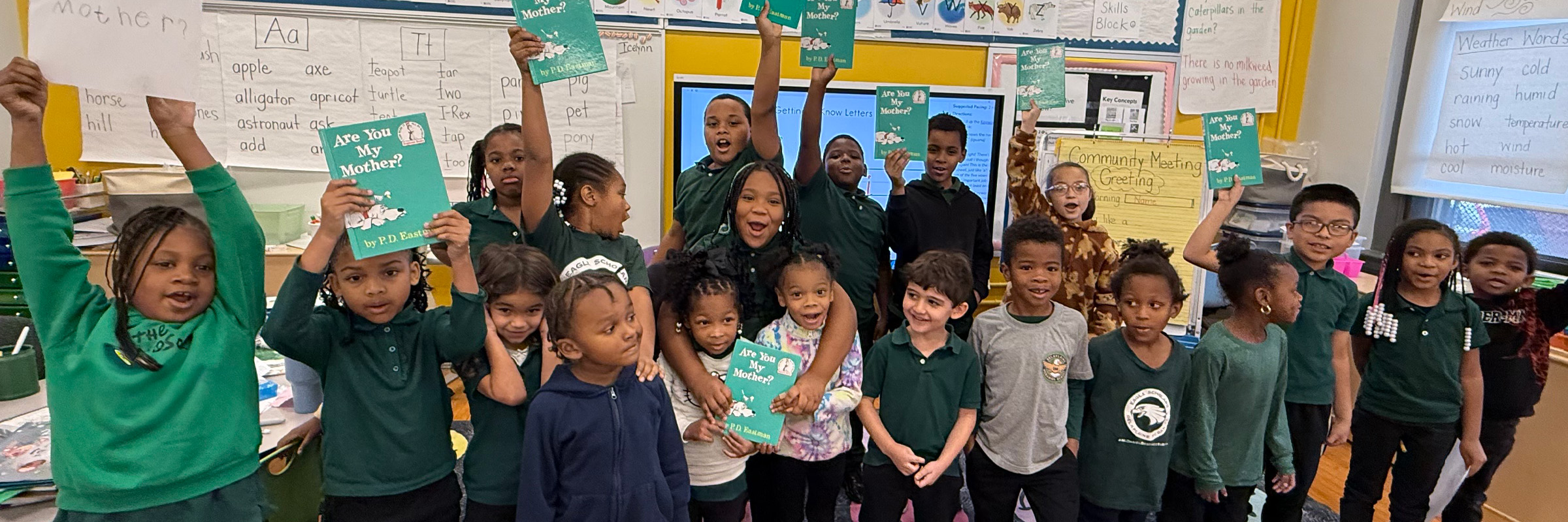 A group of elementary students stand together in a classroom holding up books during a shared reading activity at McDaniel School.